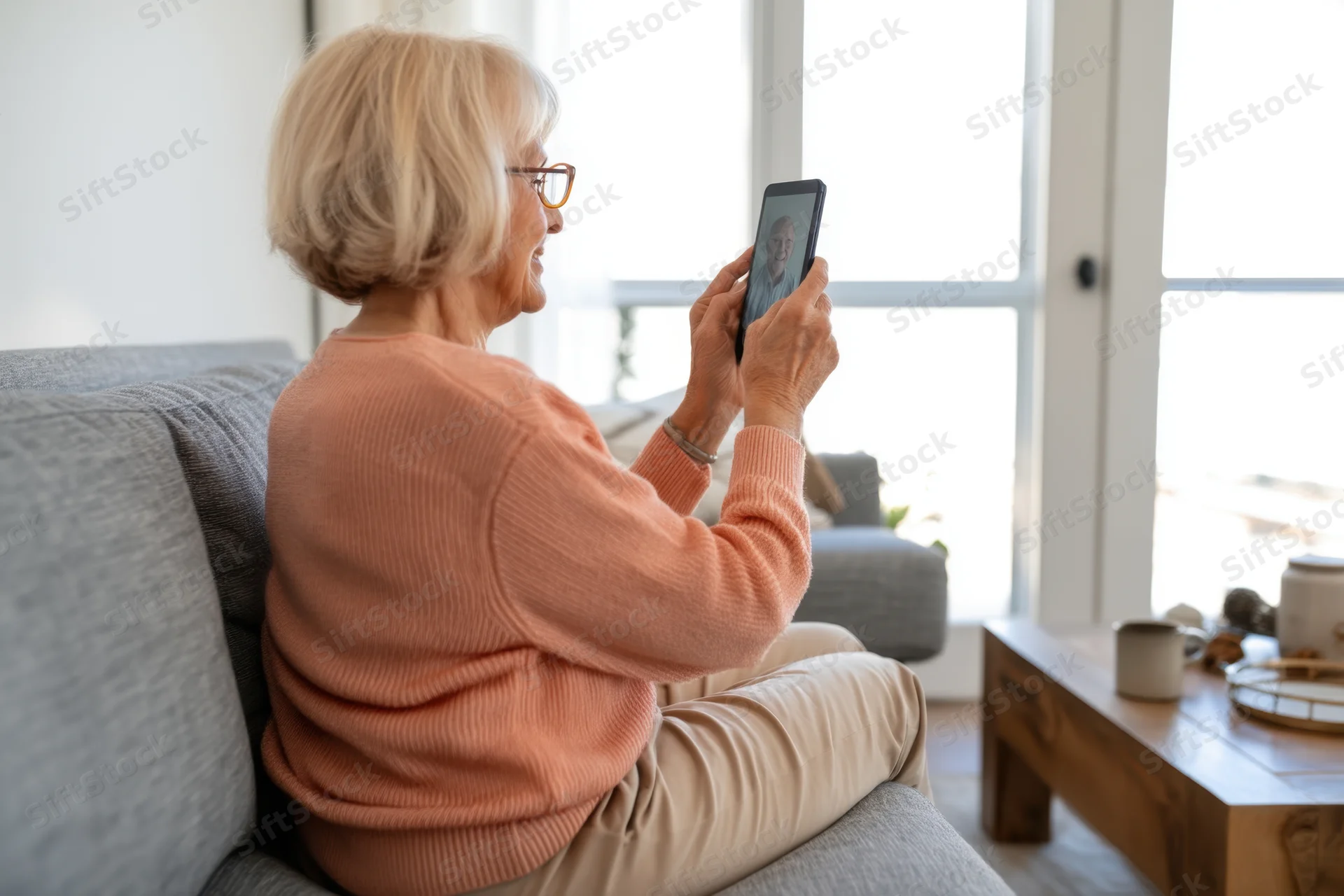 Senior woman smiling while video calling on tablet in living room