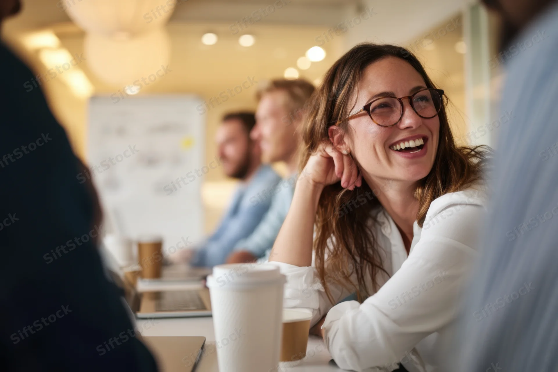 Woman laughing during office meeting around conference table with coworkers