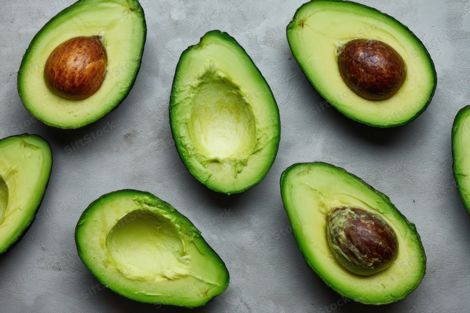Halved avocados with pits on a gray surface
