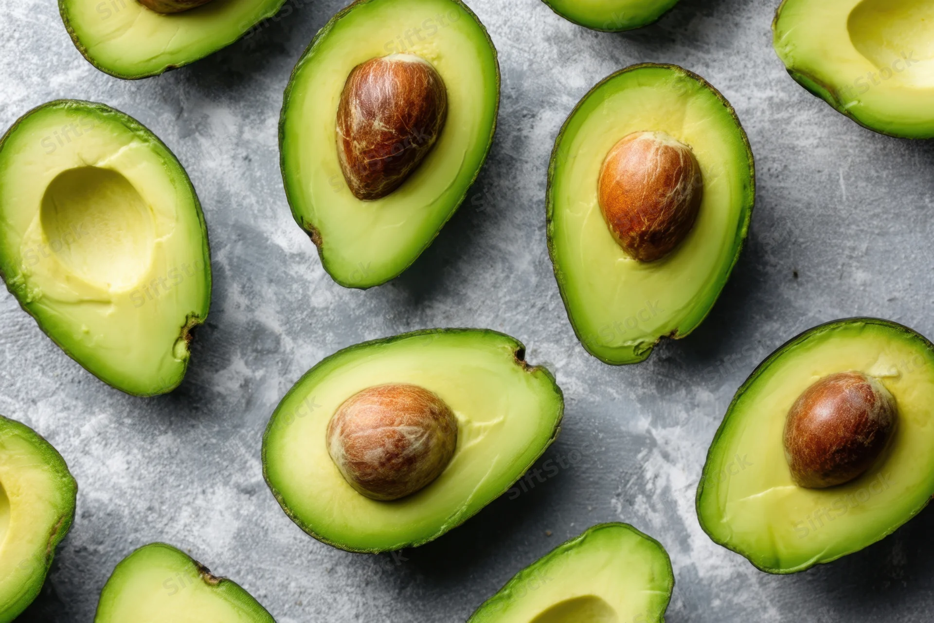 Halved avocados with pits intact arranged on a gray stone surface