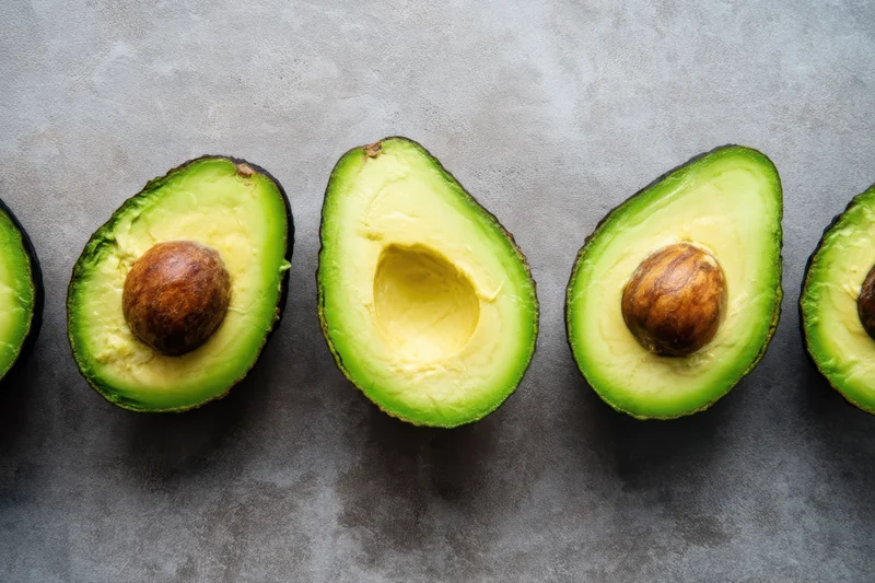 Halved avocados with pits arranged in a row on a gray surface