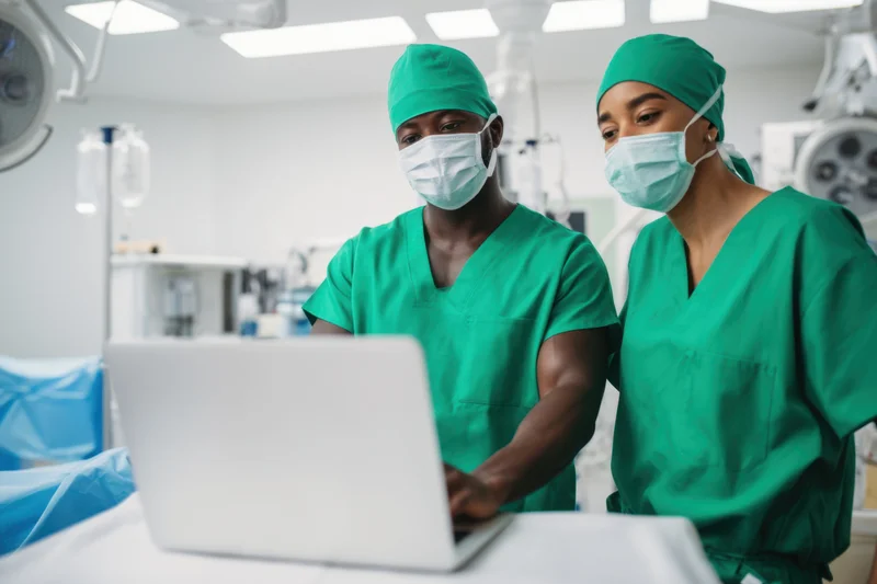 Two surgeons in green scrubs reviewing information on a laptop in an operating room