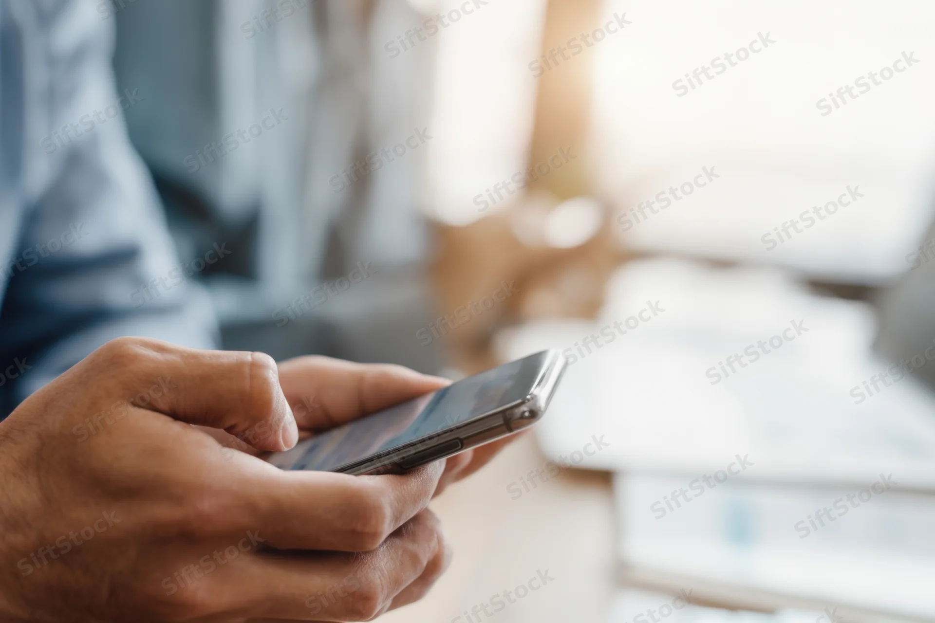 Close-up of hands holding a smartphone in a modern office workspace