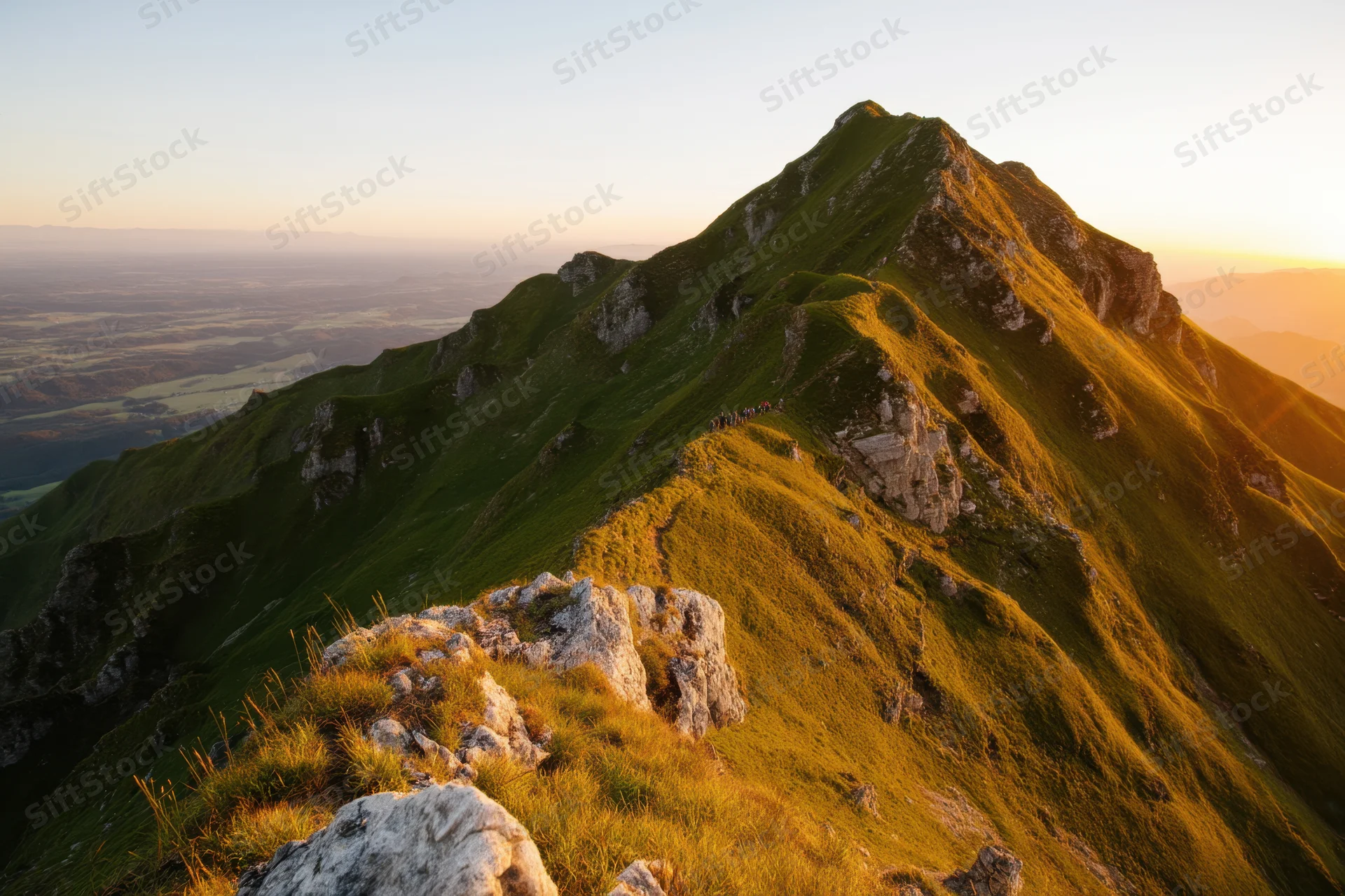 Sunlit mountain ridge with rocky outcrops and grassy slopes overlooking a valley at sunset