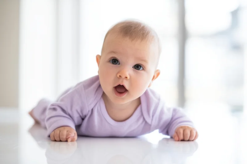 Baby lying on stomach on glossy white floor looking up with open mouth