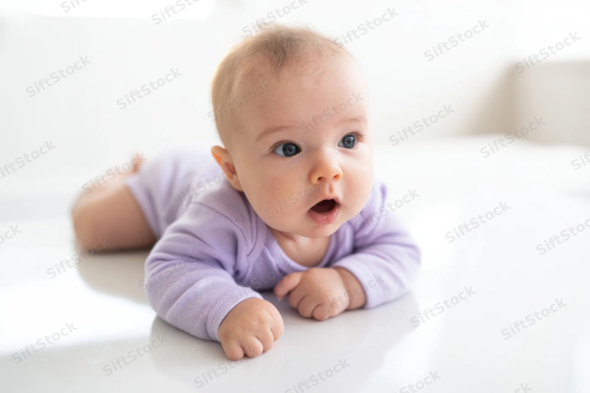 Baby lying on stomach on glossy white surface wearing purple onesie