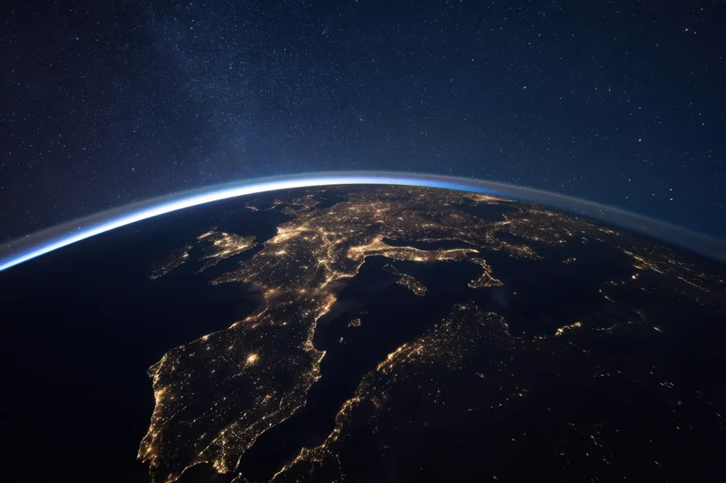 Earth viewed from orbit at night with city lights glowing against dark surface and starry sky