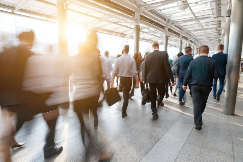 Businesspeople walking on a city sidewalk during rush hour with motion blur and sunlight flare