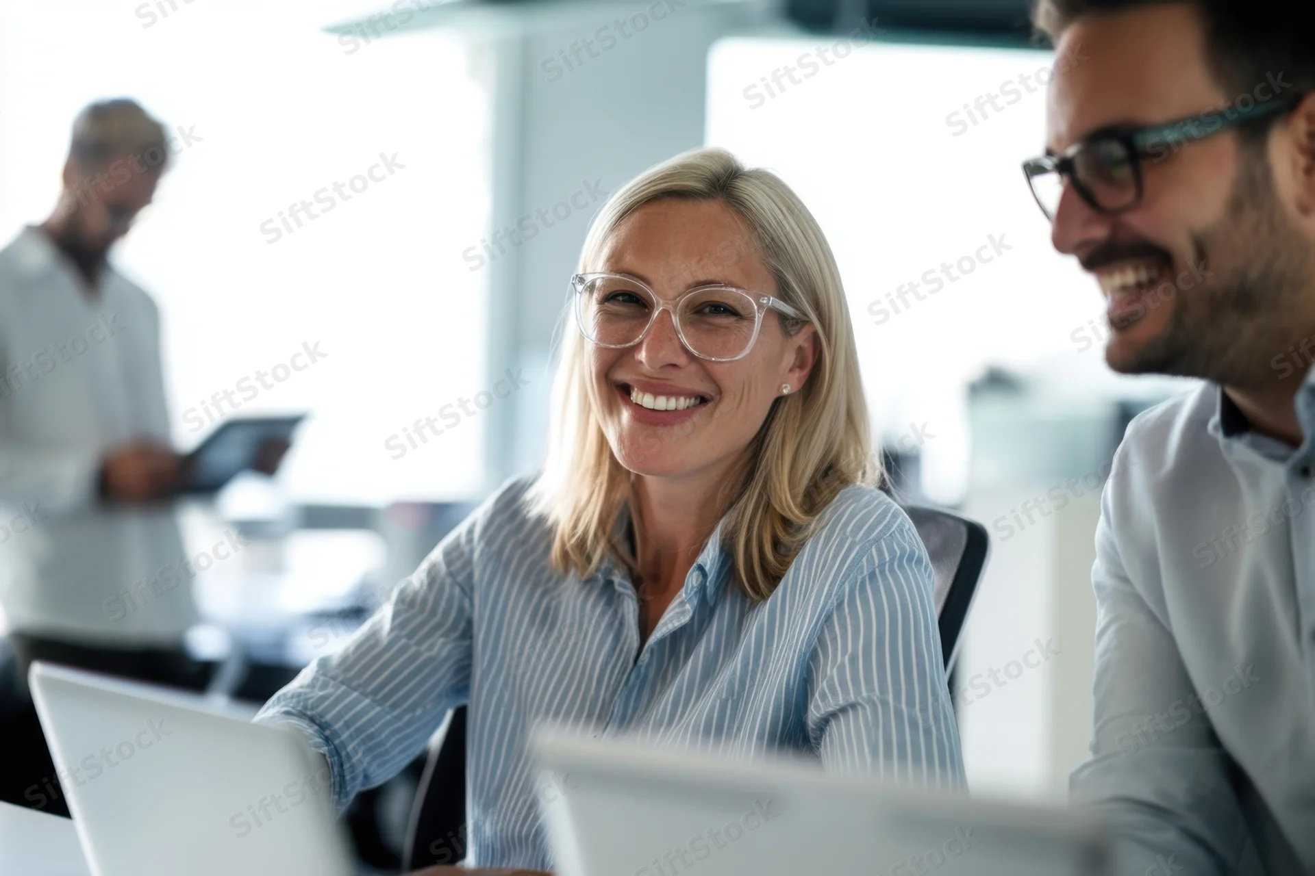 Smiling blonde woman in striped shirt working at laptop with male colleague in modern office