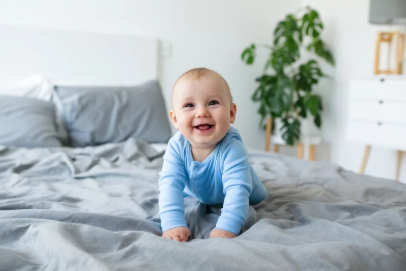 Baby crawling on gray comforter in bedroom smiling
