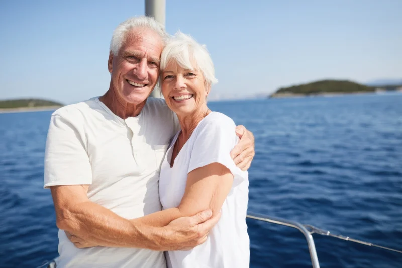 Senior couple hugging and smiling on a sailboat deck with ocean in background