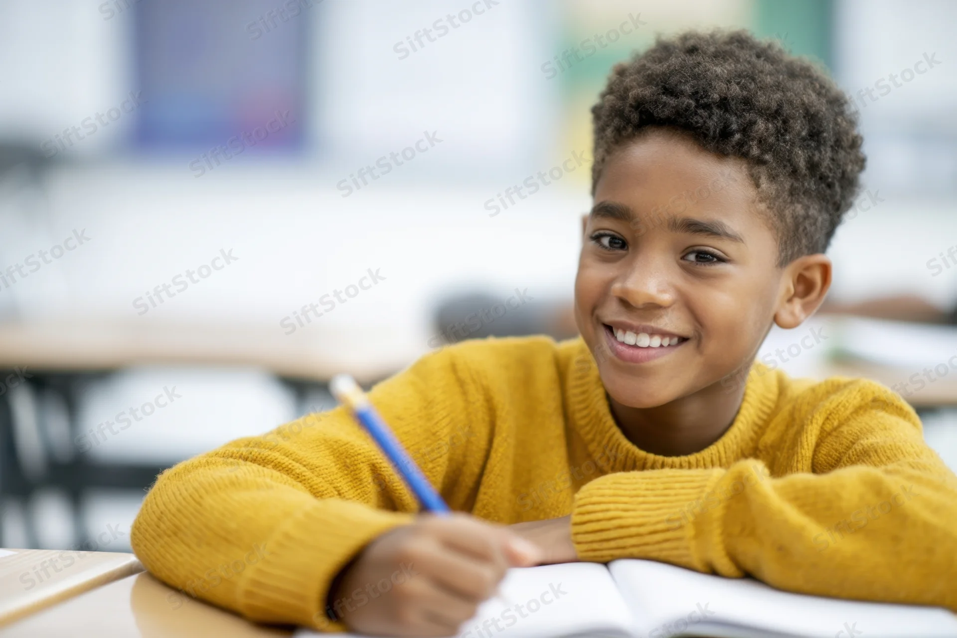 Young boy smiling while writing in a notebook at a classroom desk