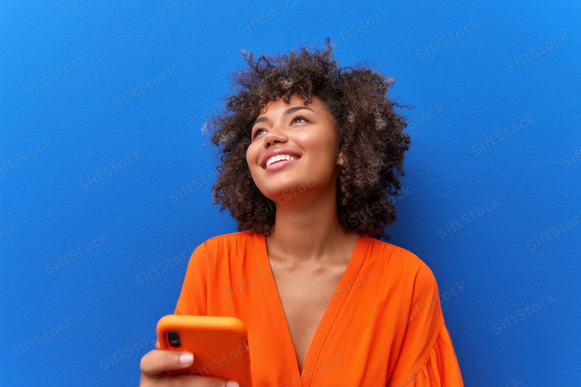 Young woman smiling while holding a phone against a blue wall