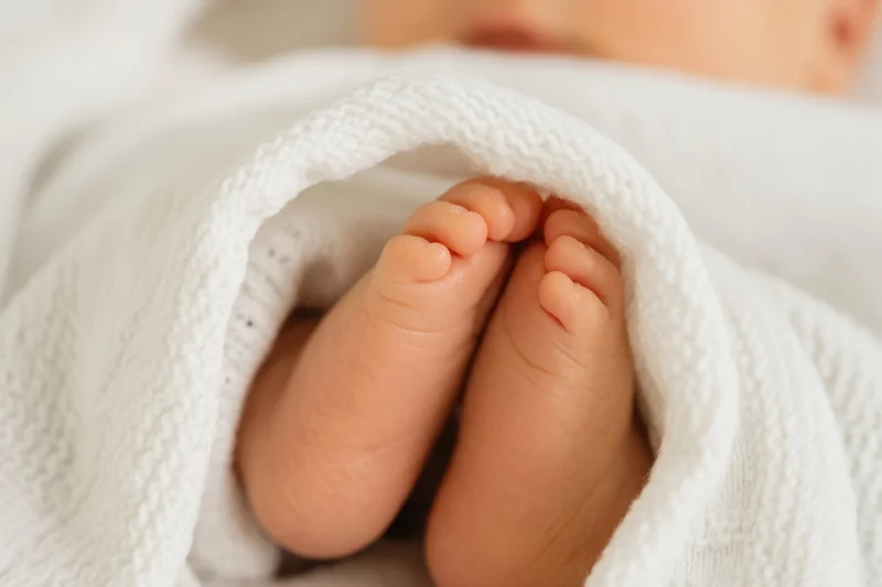 Newborn baby's feet peeking from a soft white blanket in a close-up view