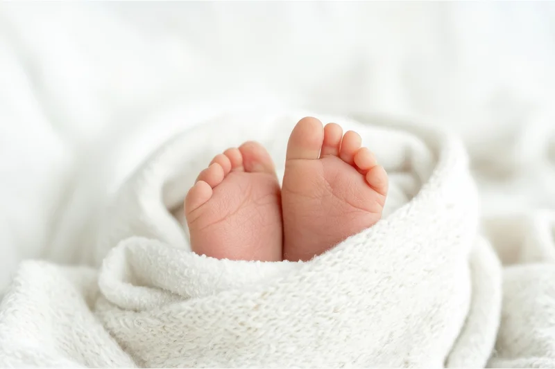 Baby's tiny feet peeking from a soft white blanket