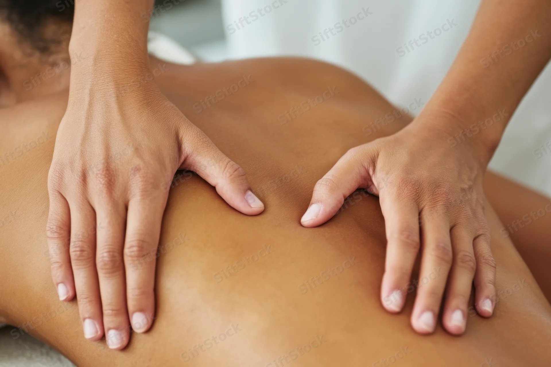 Hands massaging a bare back with fingers applying pressure in a therapy session