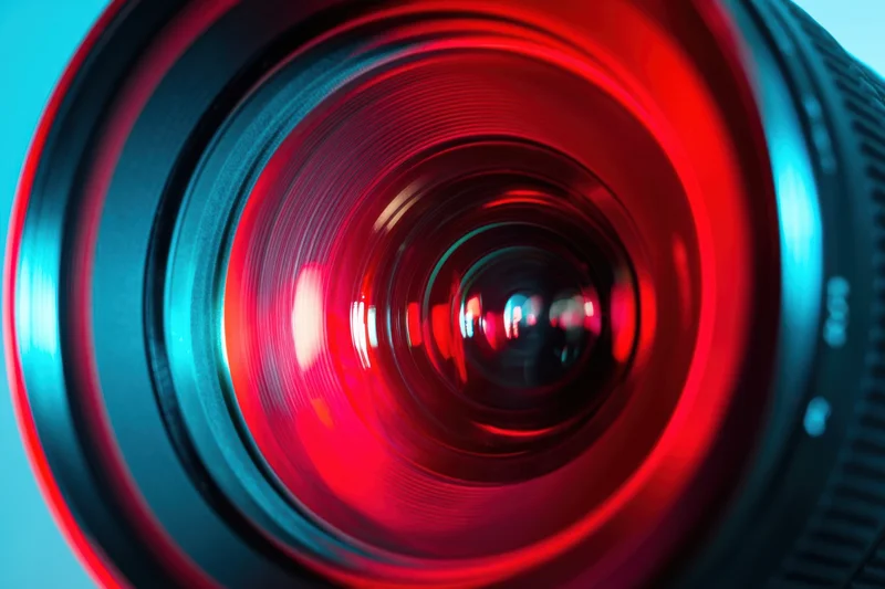 Close-up of a camera lens with red and blue neon reflections on a smooth surface