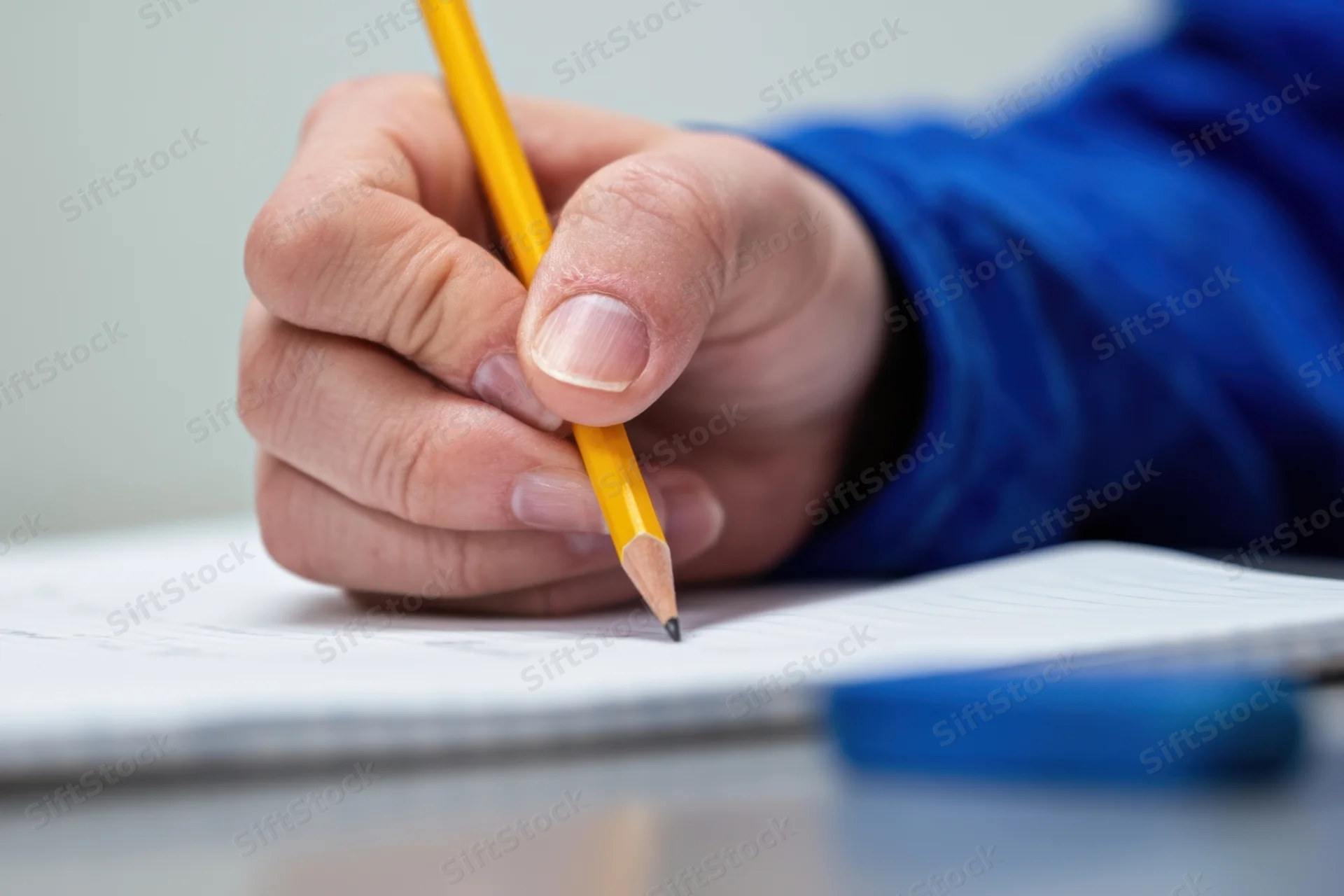 Hand holding yellow pencil writing on lined notebook paper