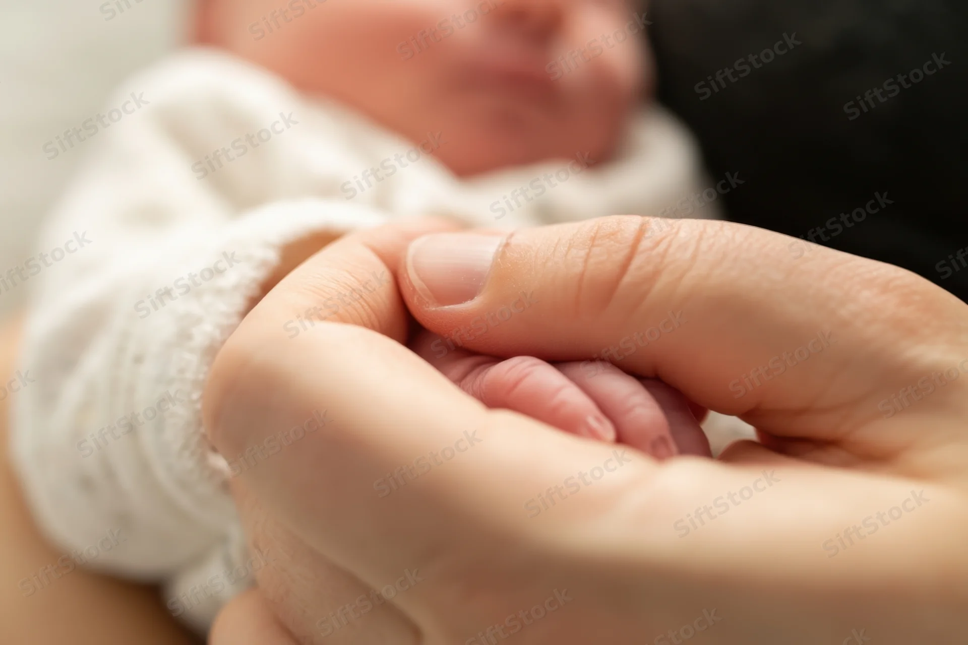 Close-up of a parent's hand gently cradling a newborn's tiny fingers