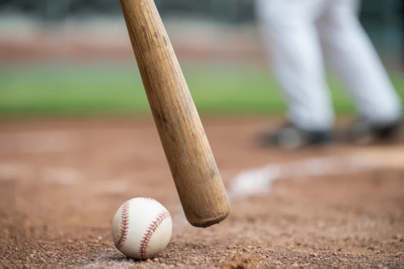 Baseball bat poised to hit a ball on the dirt near home plate during a game