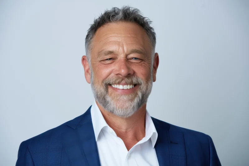 Middle-aged man smiling in a blue suit and white shirt against a plain background