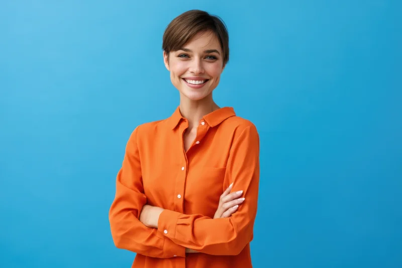 Confident woman smiling with arms crossed in orange shirt against blue background