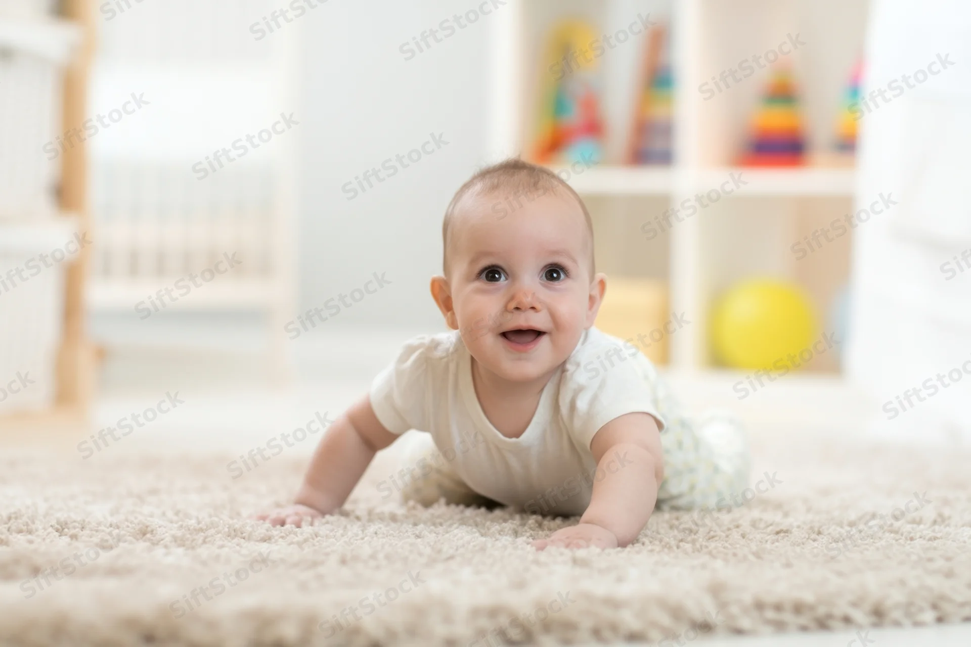 Baby crawling on soft beige rug in bright playroom with toys on shelf