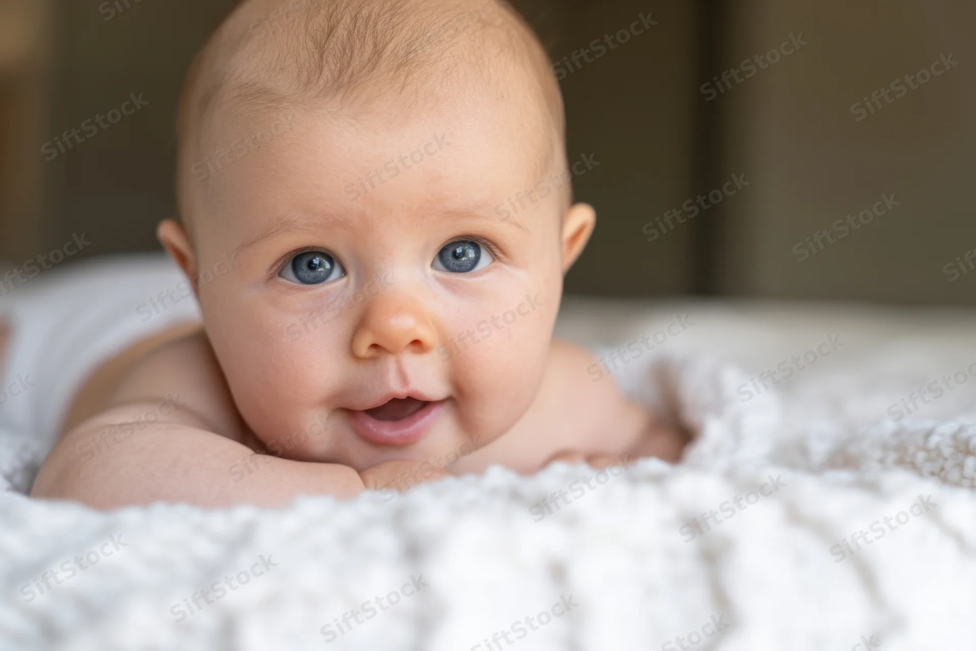 Baby lying on stomach on white textured blanket indoors smiling with blue eyes