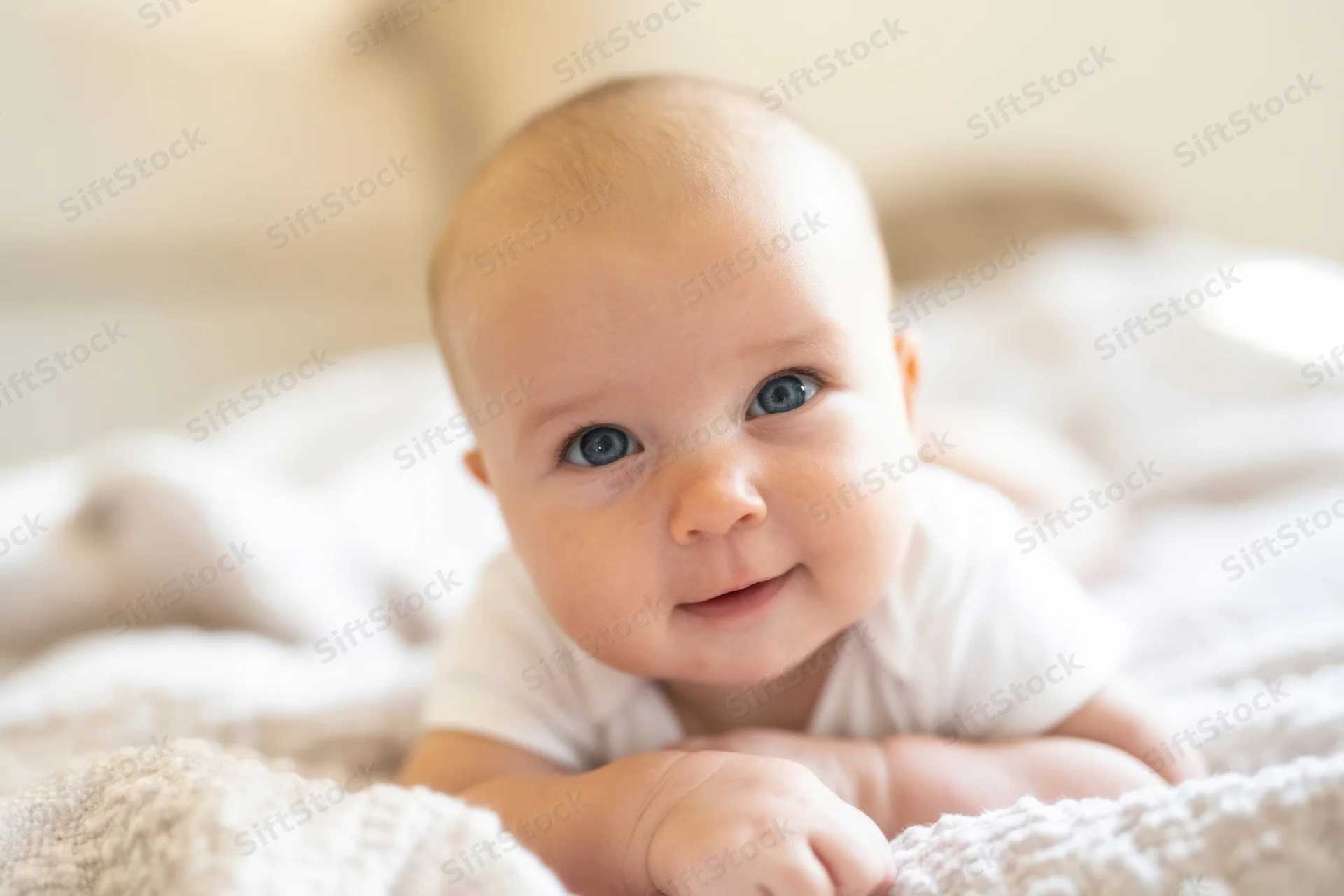 Baby lying on tummy on soft textured blanket in bedroom