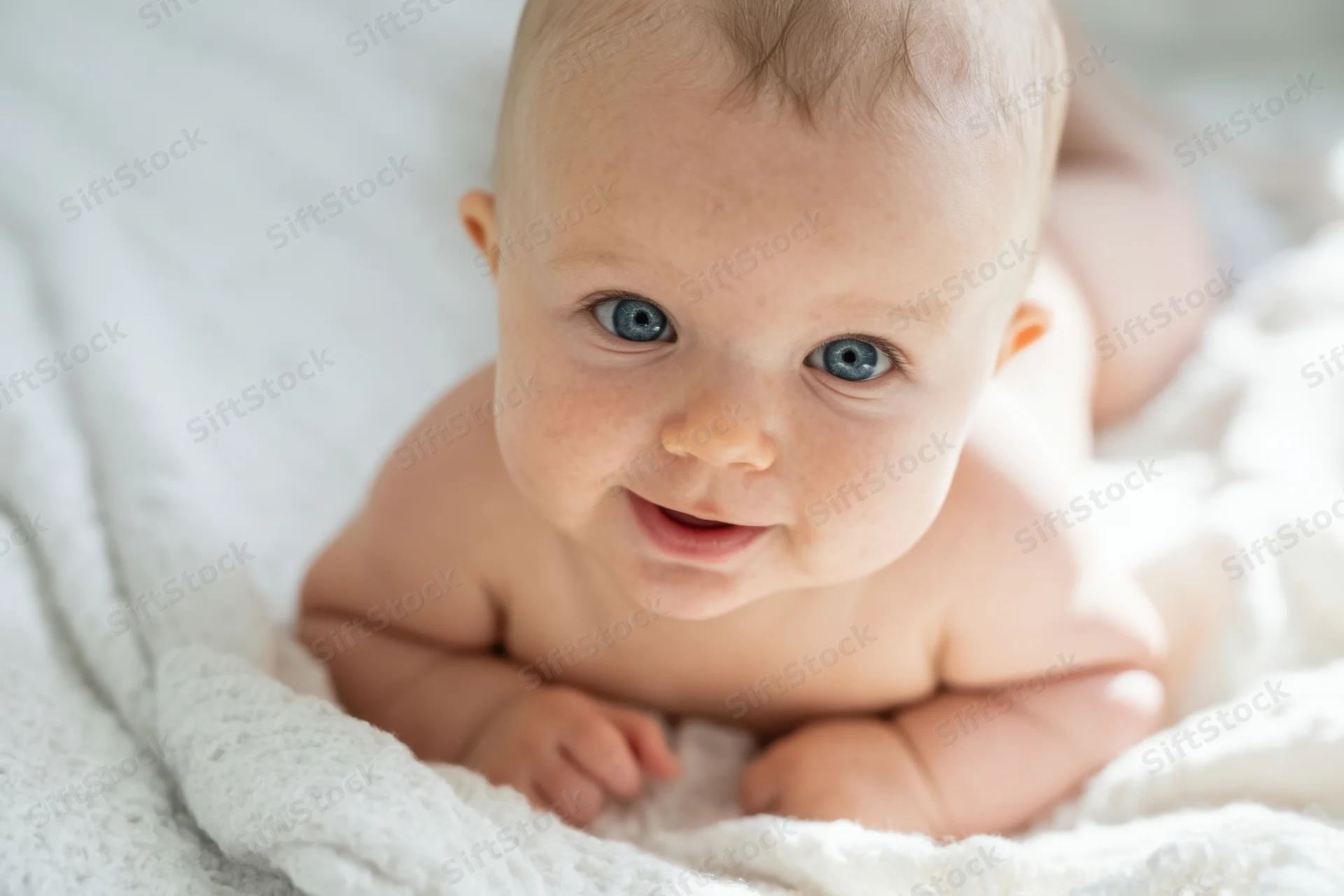 Baby lying on stomach on white textured blanket smiling at camera