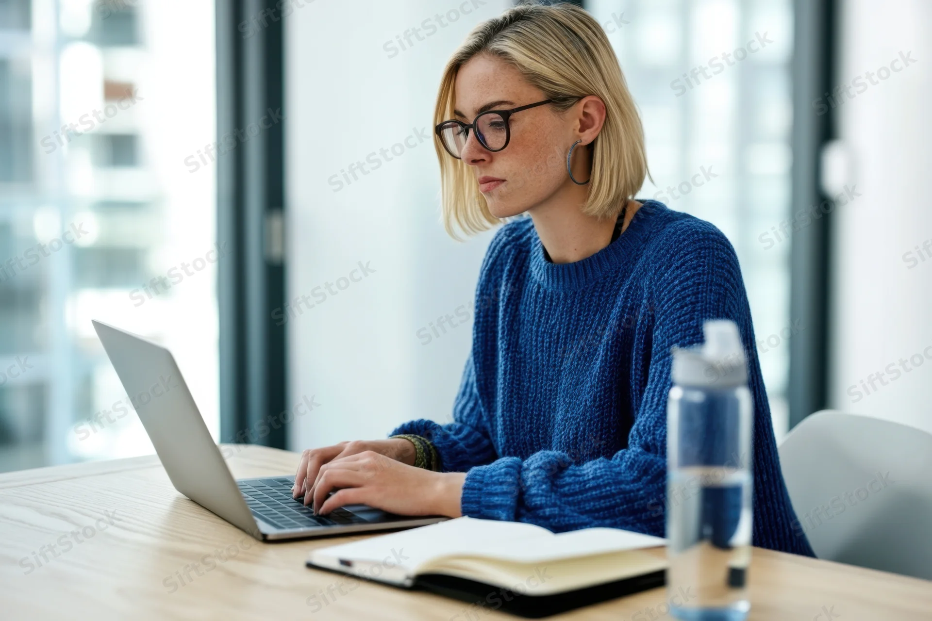 Woman typing on laptop at wooden desk in modern office workspace