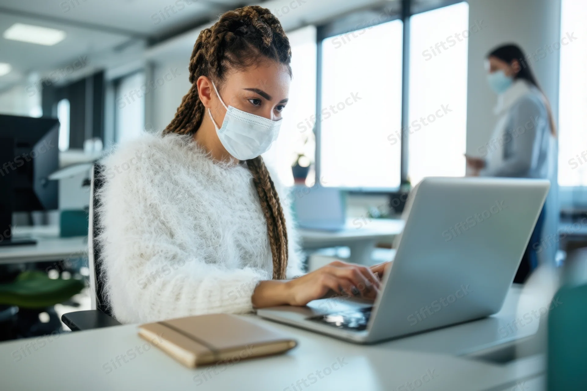 Woman typing on laptop at office desk wearing face mask