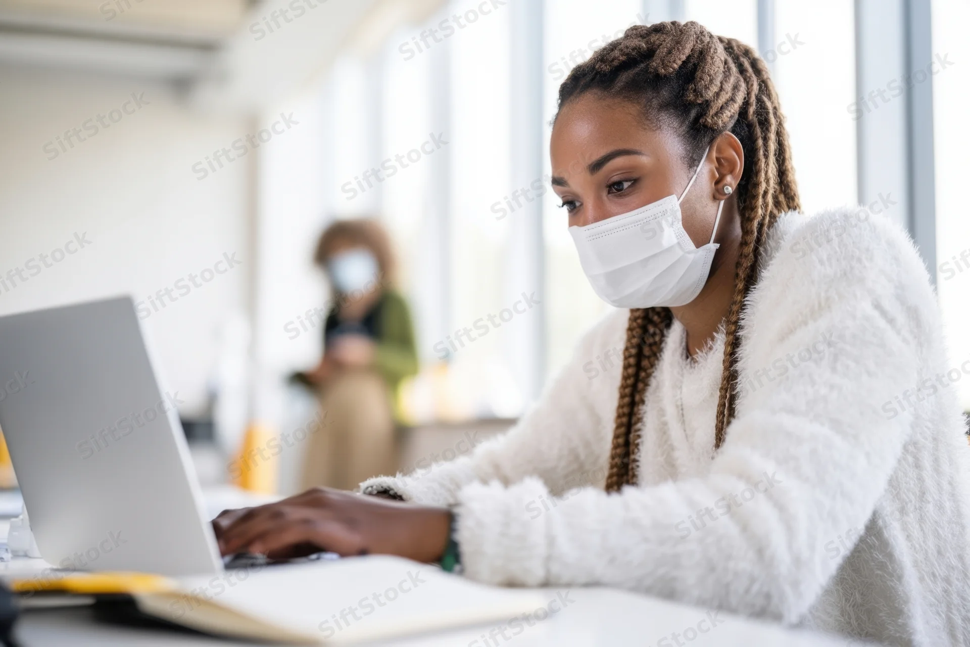 Woman wearing mask typing on laptop at office desk