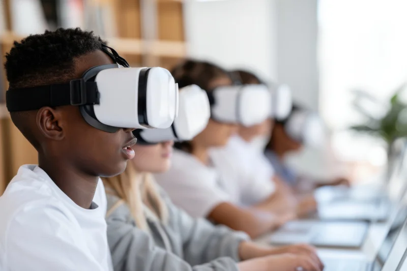 Children wearing vr headsets seated in a row at desks in a bright classroom
