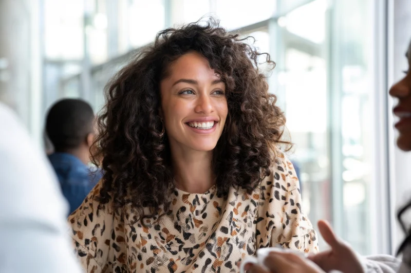 Smiling black woman with curly hair engaged in conversation at a cafe table