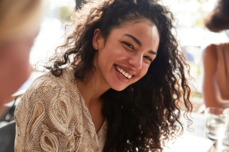 Young black woman smiling at cafe table with friends during daytime social gathering