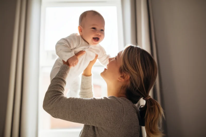 Mother lifting baby into air by window in sunlight