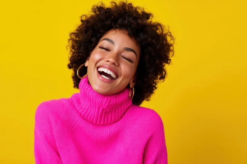 Woman laughing with eyes closed wearing bright pink turtleneck sweater against yellow background
