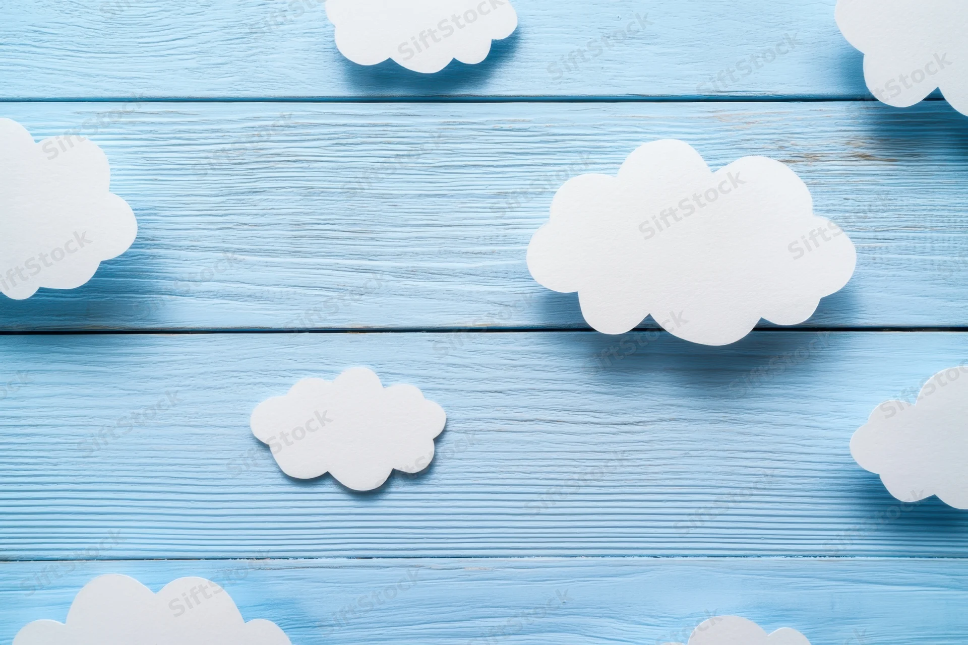 White paper clouds arranged on a light blue wooden panel surface
