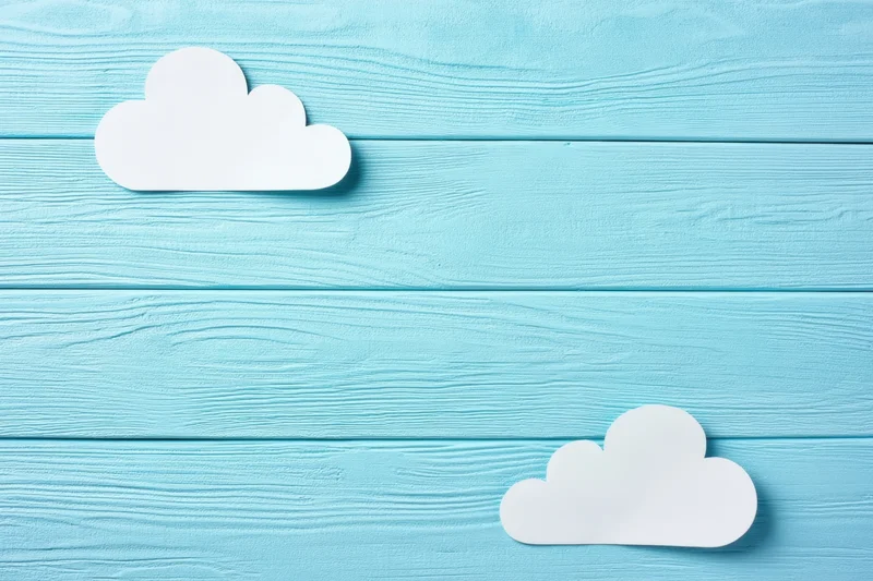 White paper clouds on light blue wooden panel background