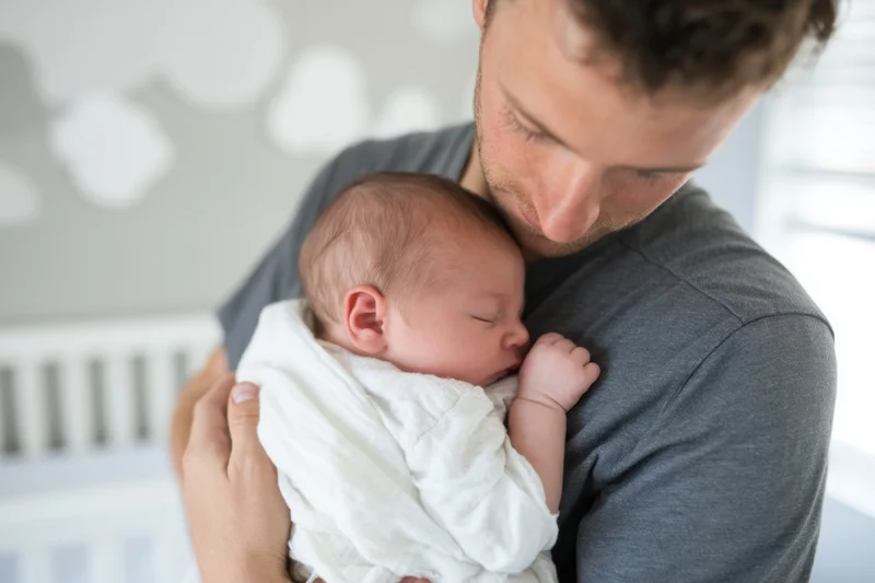 Father cradling sleeping newborn close to his chest in nursery