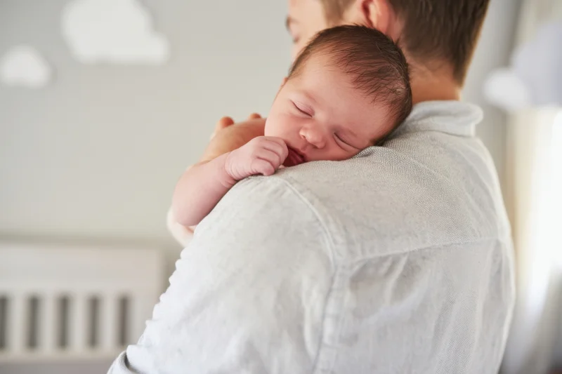 Father holding sleeping newborn close to his chest in a nursery