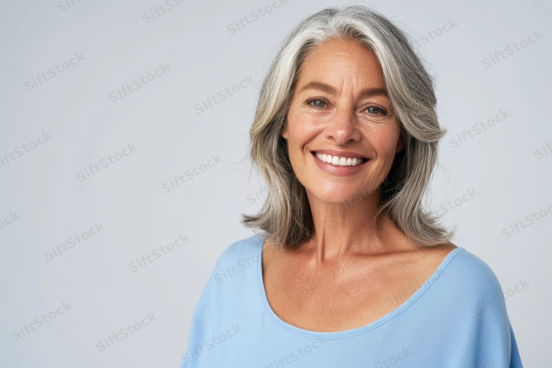 Mature woman smiling in a studio portrait with shoulder-length gray hair and a blue top
