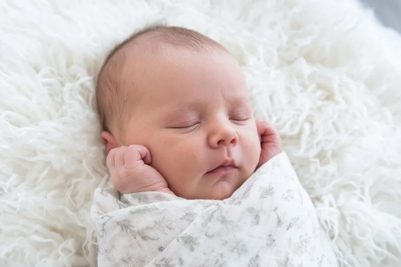 Newborn baby sleeping swaddled in a white fluffy blanket