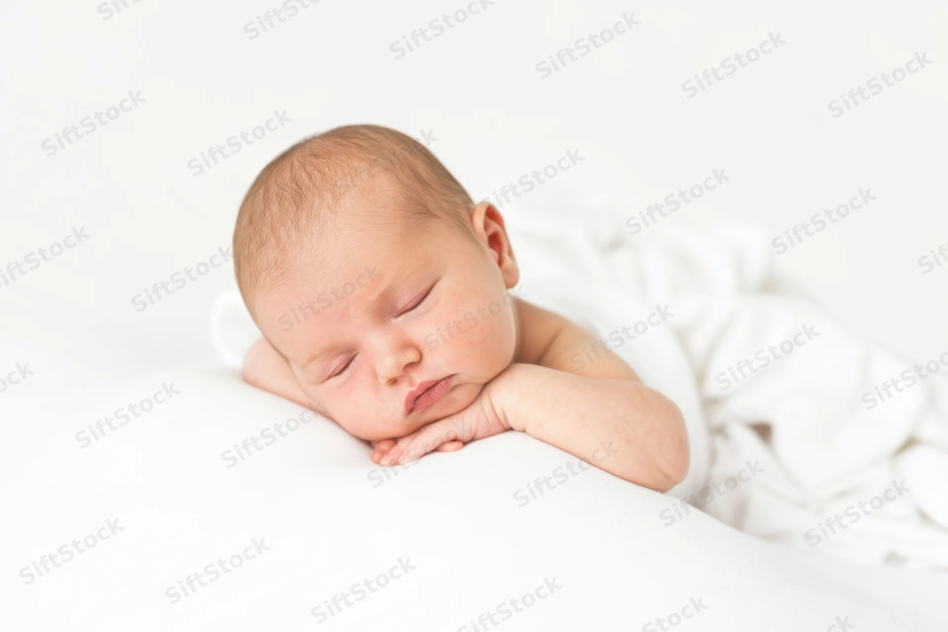 Newborn baby sleeping peacefully on a white blanket with head resting on hand