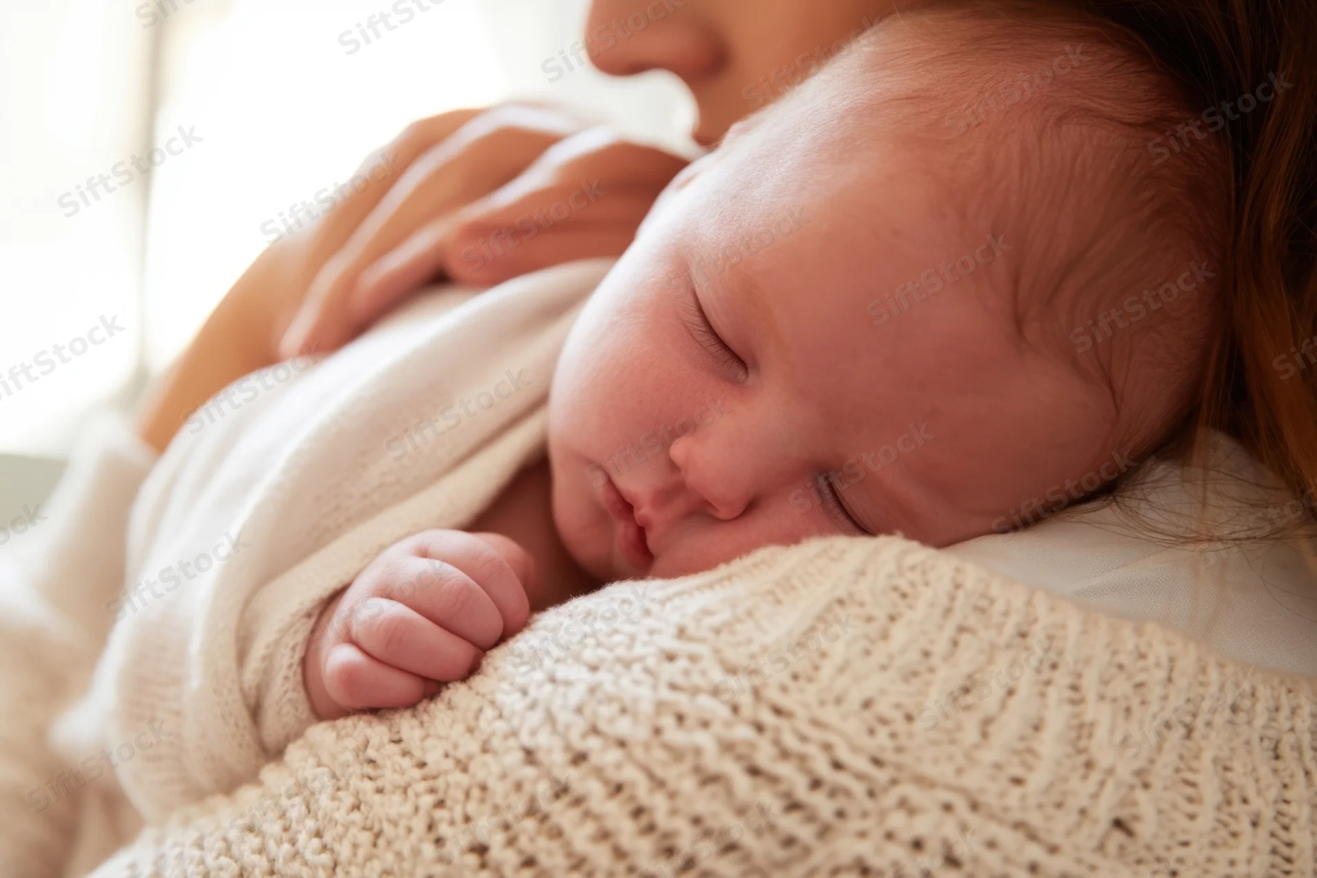 Newborn sleeping on mother's shoulder wrapped in soft knitted blanket