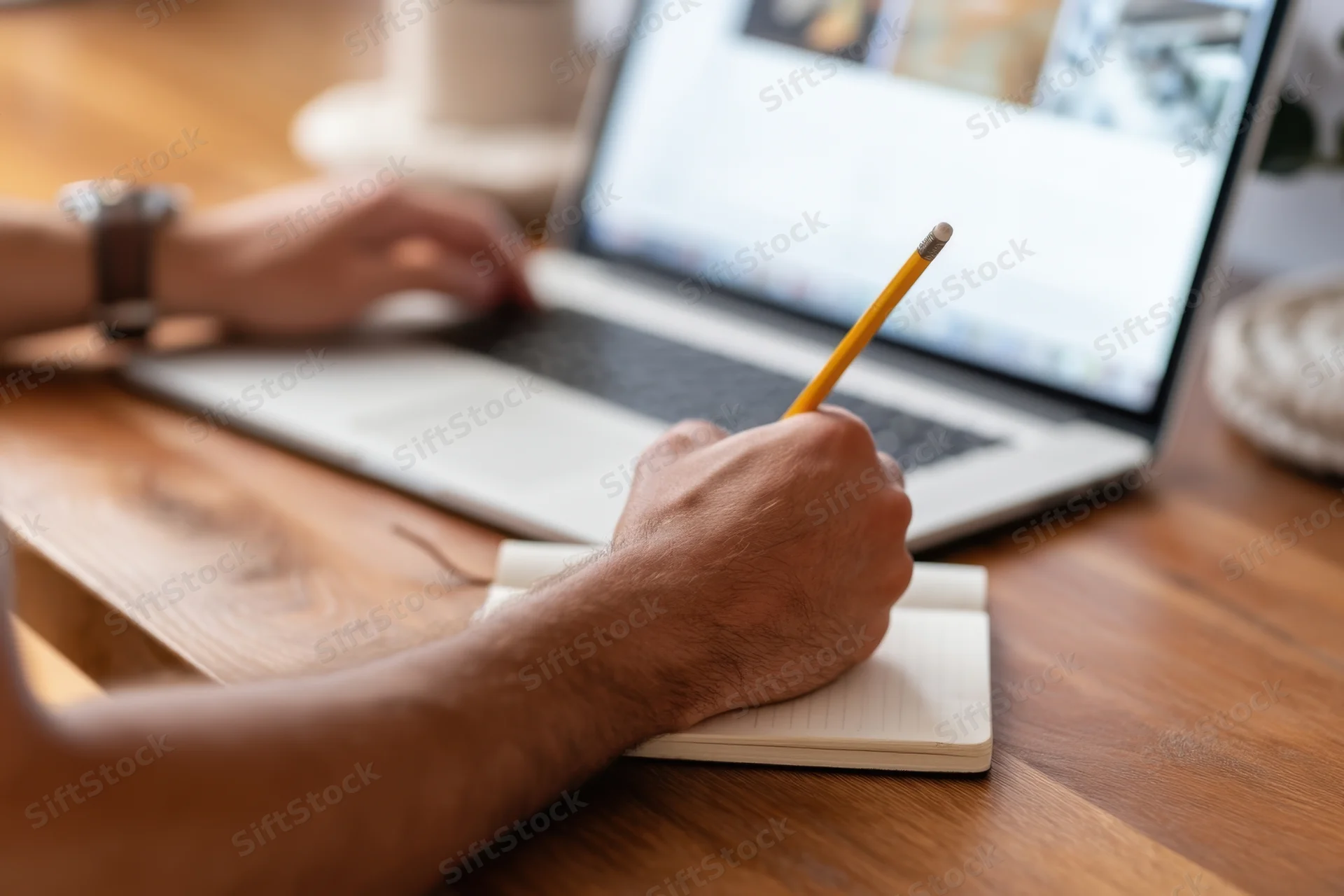 Man writing in notebook with laptop on wooden desk