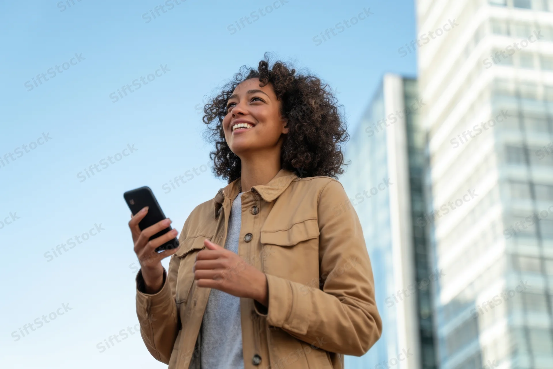 Woman smiling while holding smartphone outdoors in city setting