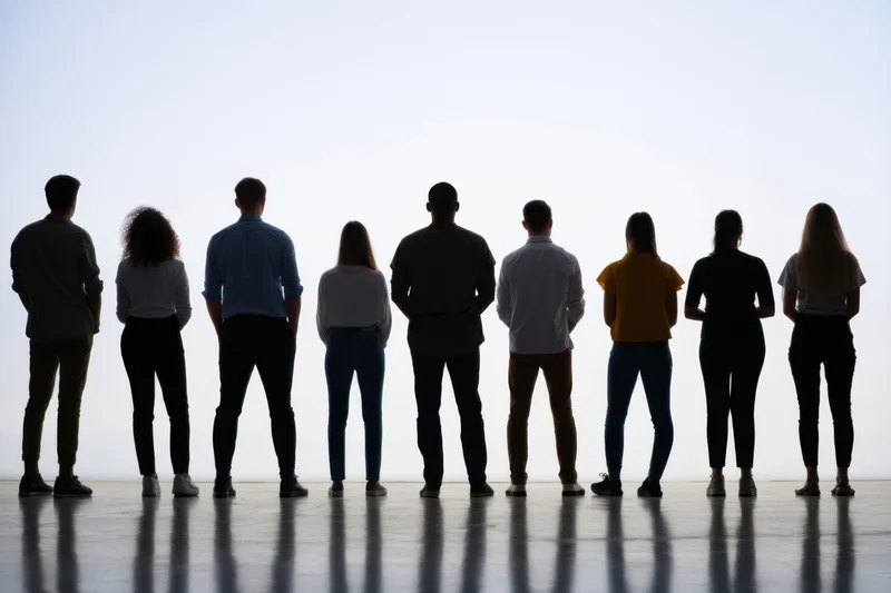 Diverse group of people standing in a row with backs to camera in a bright studio