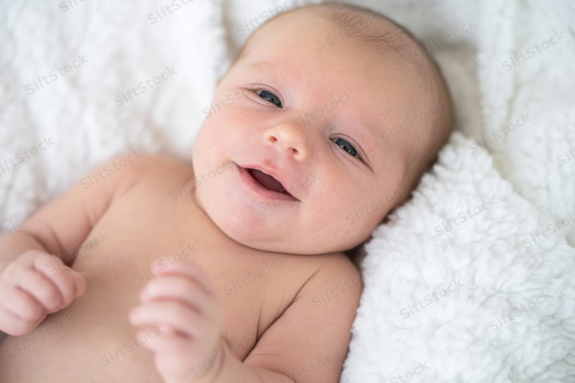 Smiling newborn lying on white plush blanket in soft daylight